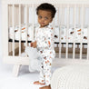 toddler in safari jammies standing in front of wood crib with safari animal print silk crib sheets 